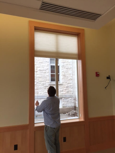 person looking up at a window shade pulled up over a large window